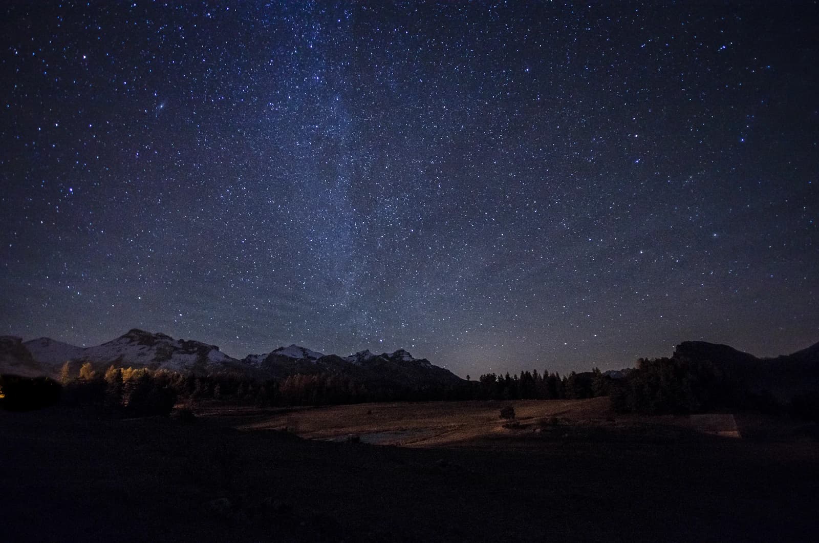 Starry night sky with the Milky Way above a mountain ridge and open meadow
