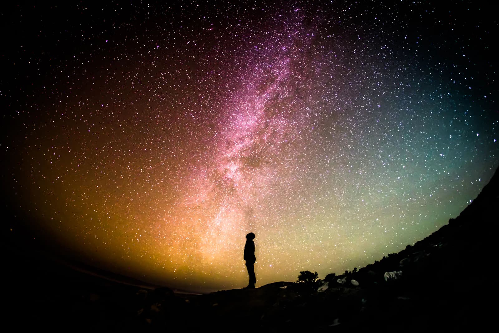 Silhouette of a person standing beneath a pink and green Milky Way
