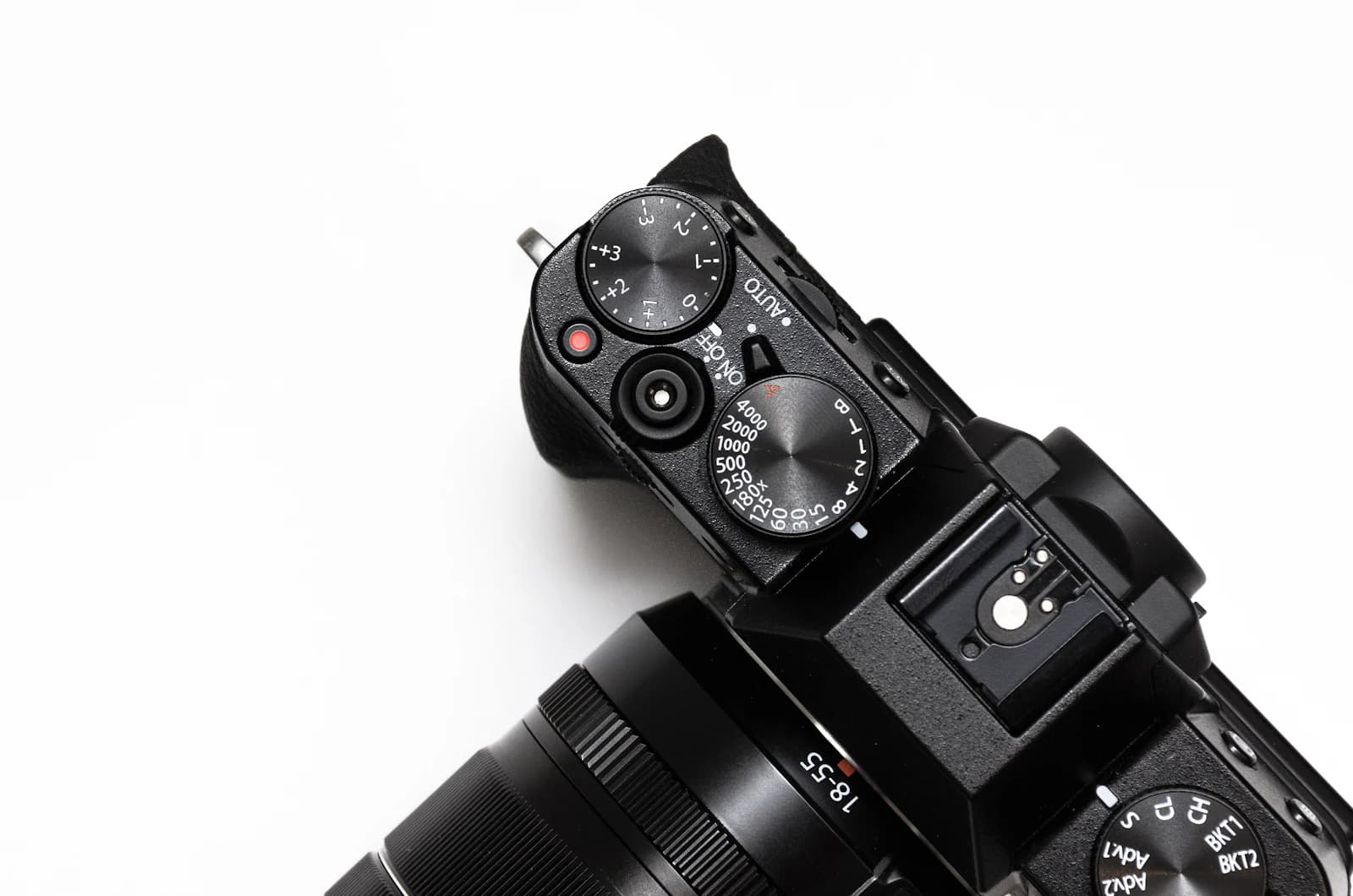 Top of a camera with dials and lens photographed against a white background