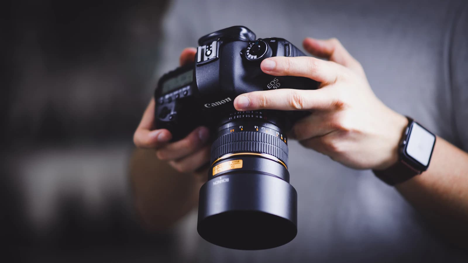 Two hands holding a DSLR camera with a lens attached