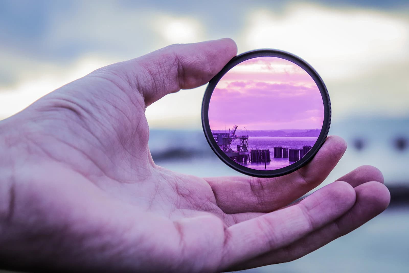 Hand holding a filter ring that frames a purple sunset scene