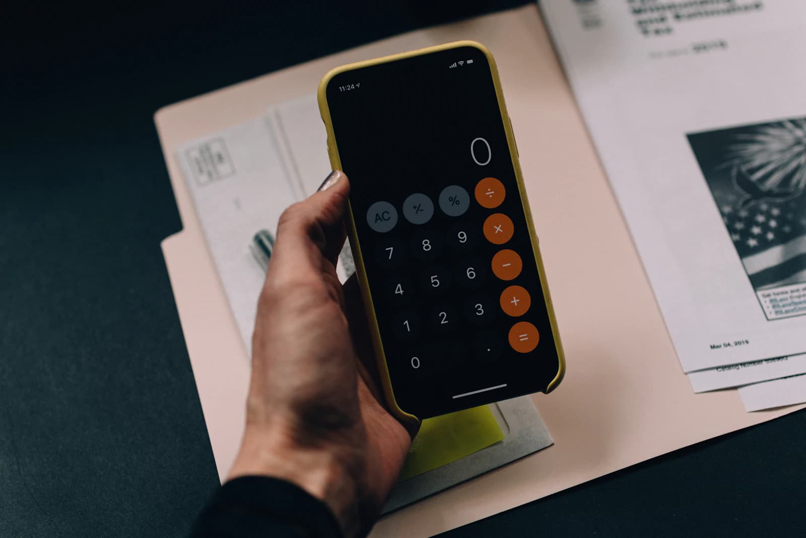 Hand using a smartphone calculator over a pile of papers