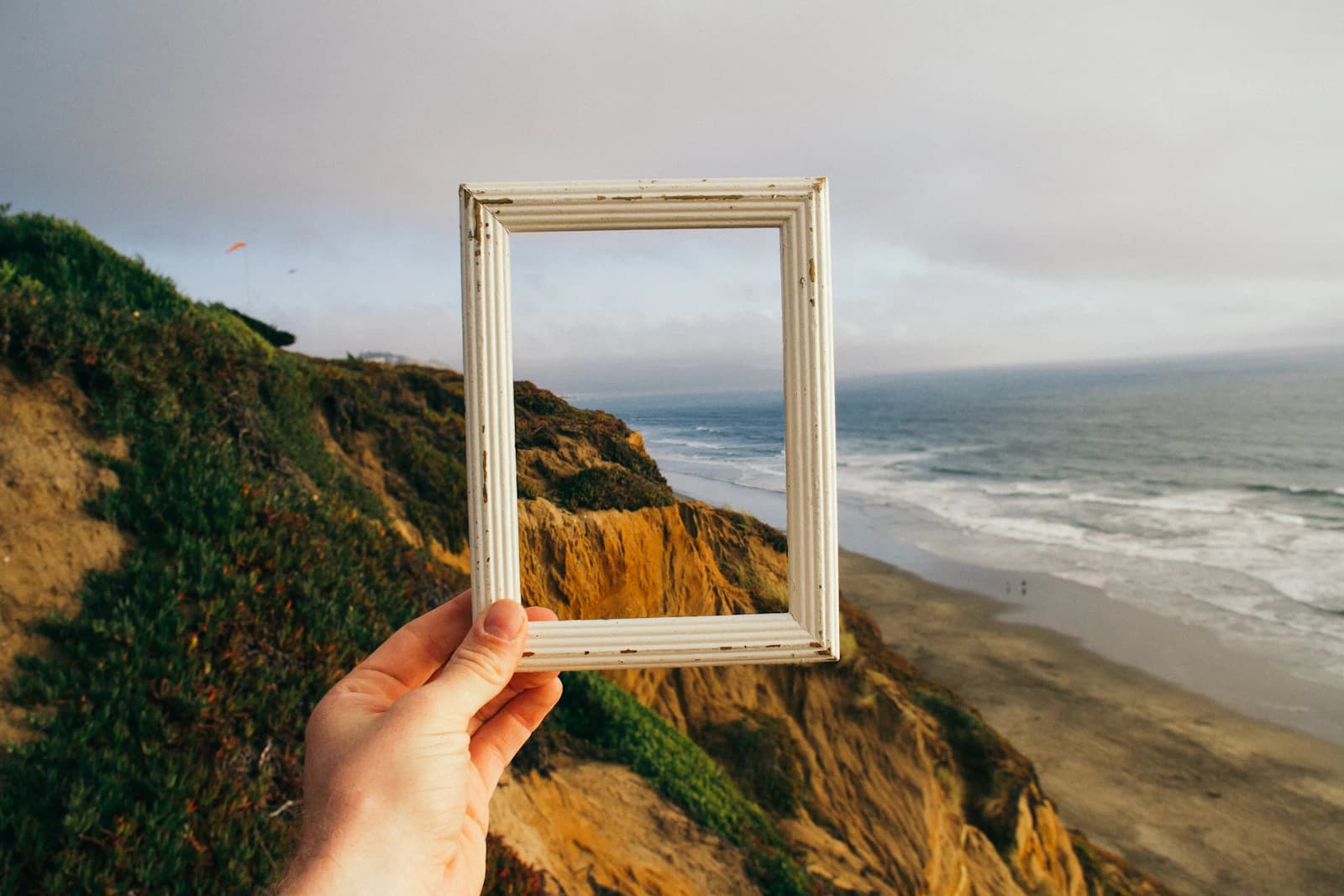 Hand holding an empty picture frame in front of a coastal cliff and sea