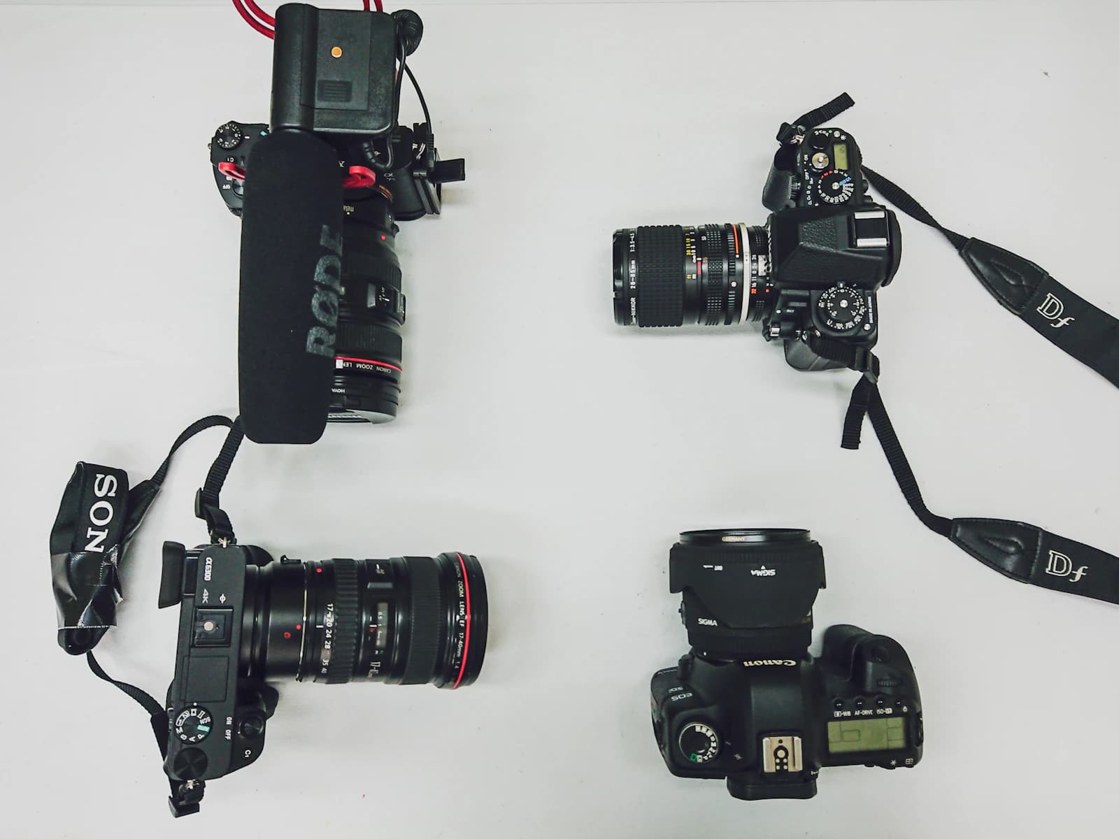 Four cameras with straps laid out on a white surface