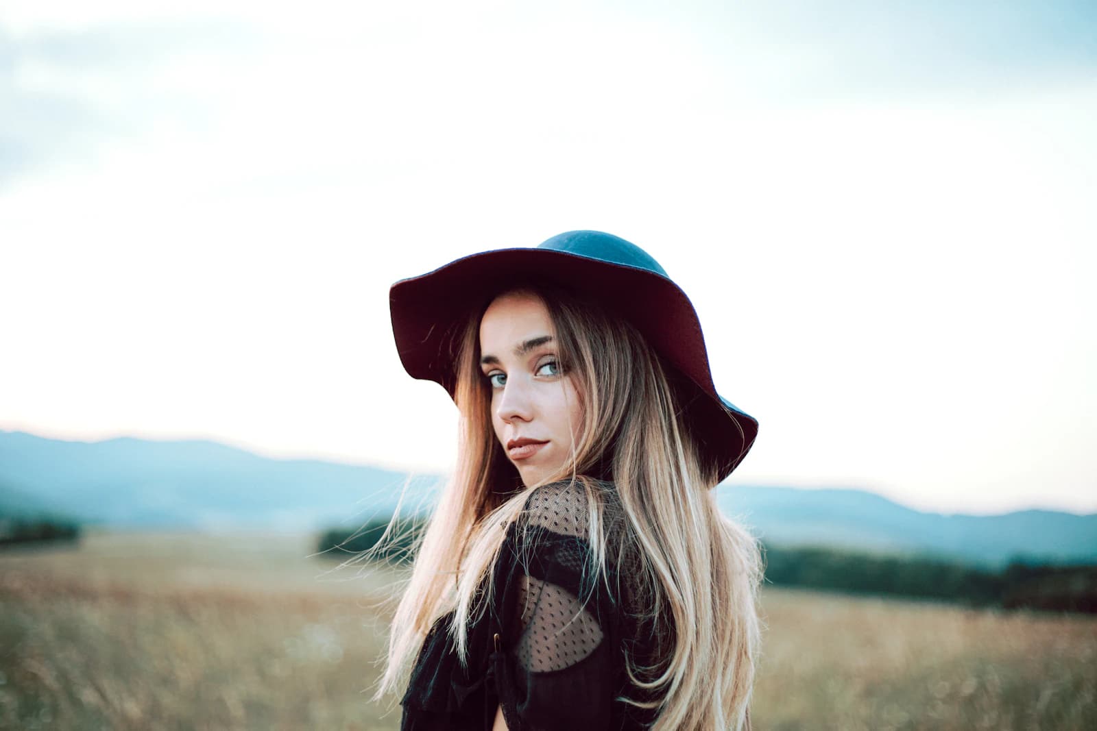 Portrait of a woman in a hat looking back in an open field