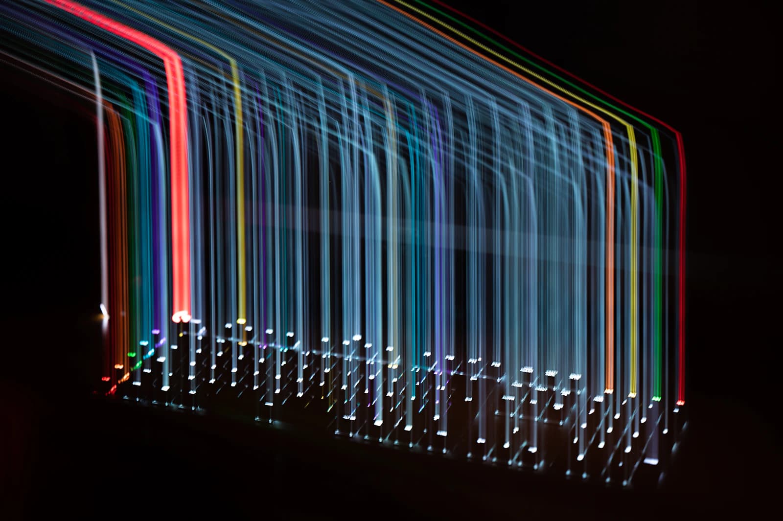 Long-exposure photo of multicolored light streaks hanging vertically on a black background