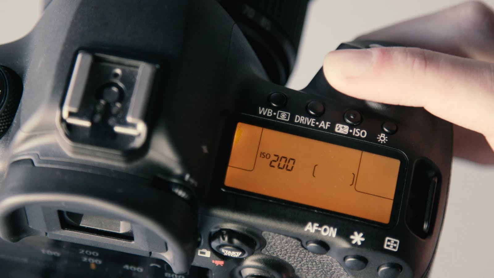 Camera top LCD showing ISO 200 with a finger pressing a button