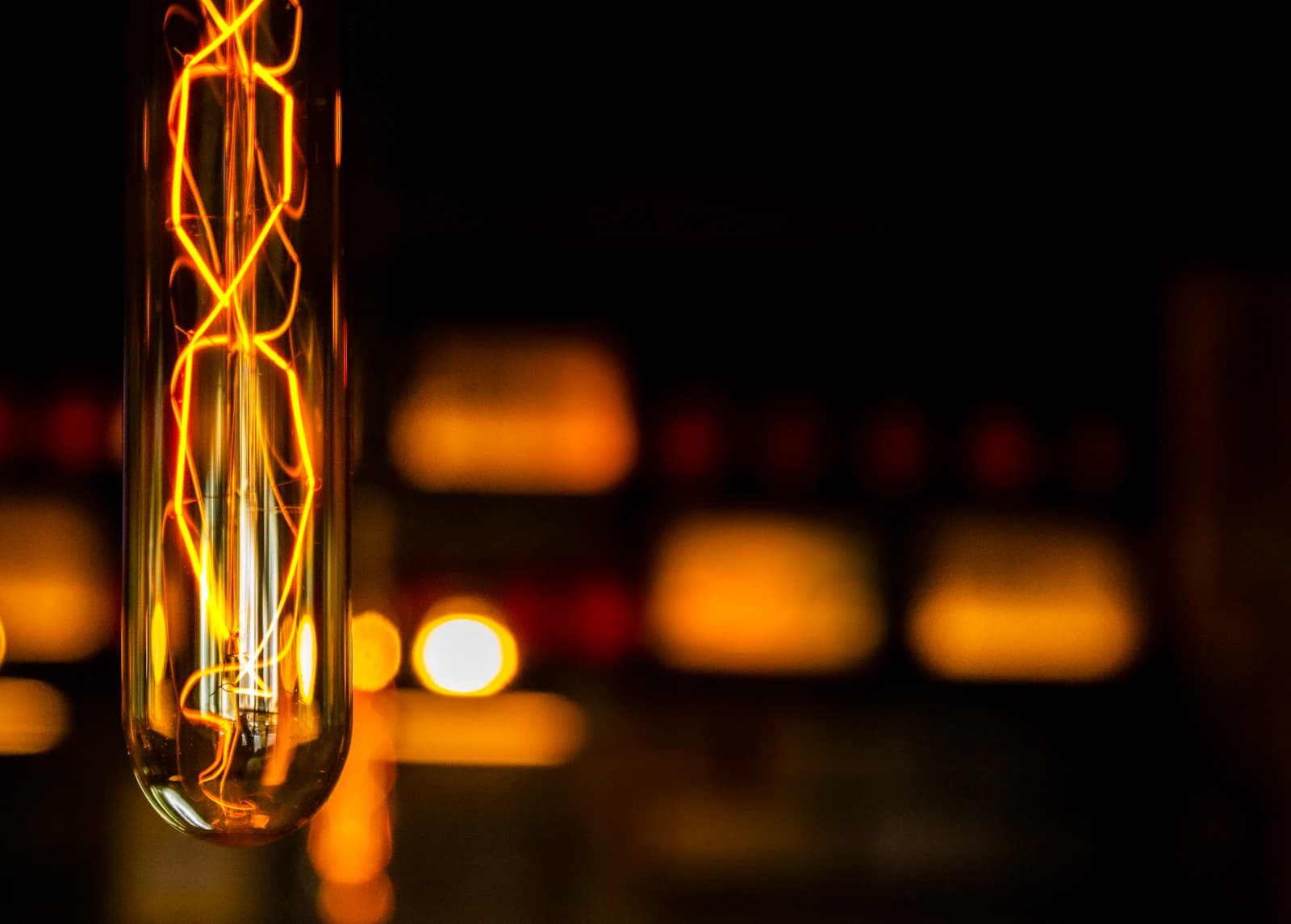 Glowing filament bulb with blurred warm lights in the dark background