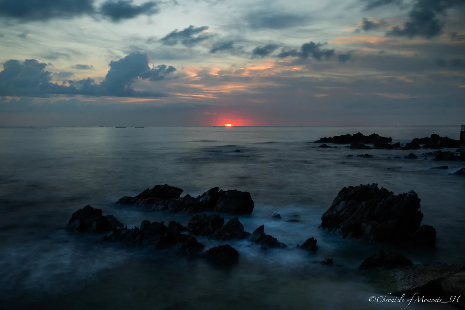 Long-exposure seascape at sunrise with silky water around dark rocks