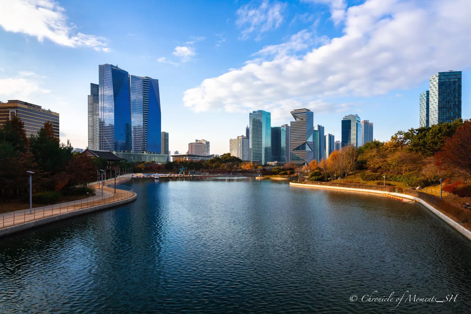 Skyscrapers beside a calm lake under a blue sky